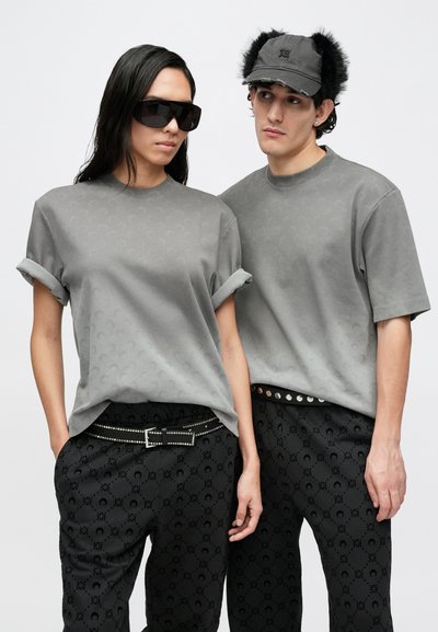 Gray cotton t-shirts, rolled sleeves, patterned with a subtle logo. Black pants feature a repeating pattern, adorned with a studded belt.