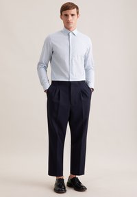 Hellblaues Hemd mit kleinen weißen Polka-Dots, kombiniert mit marineblauen, plissierten Hosen und schwarzen Schnürschuhen. Glatter Stoff, maßgeschneiderte Passform.