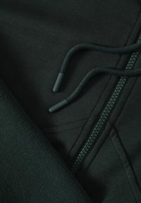 Tejido de sudadera de color verde oscuro con una textura suave, que cuenta con un cierre de cremallera y cordones con puntas de goma.