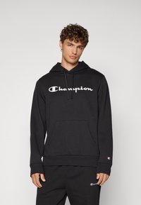 Haut à capuche noir Champion avec une poche avant, cordons de serrage et logo blanc. Fabriqué en tissu doux, il possède des poignets et un ourlet côtelés.