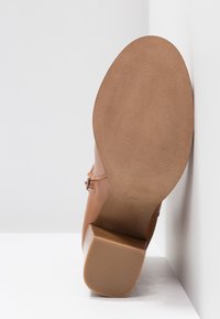Chaussure à talon en cuir marron avec dessus lisse, semelle extérieure texturée et talon carré épais. Dispose d'une boucle latérale en détail.