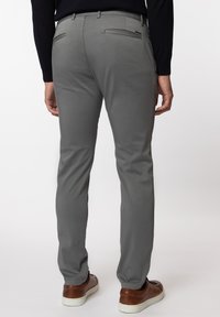 Graue Chinos mit Slim-Fit, ausgestattet mit Seiten- und Gesäßtaschen sowie einer glatten Stofftextur. Dazu werden braune Schuhe getragen.