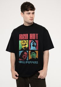 Black oversized t-shirt featuring a colorful graphic print of four band members with the text “RED HOT CHILI PEPPERS” at the bottom.