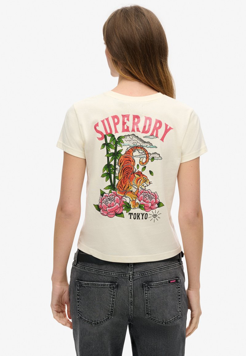Kremno obarvana majica s kratkimi rokavi, na hrbtni strani z barvitim motivom tigra in cvetja ter napisom "SUPERDRY TOKYO" zgoraj.