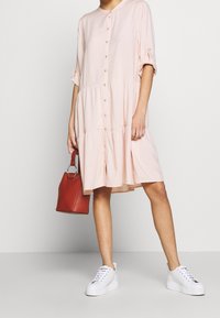 Abito rosa chiaro, con bottoni sulla parte anteriore, design a strati, maniche corte e scollatura rotonda. Abbinato a scarpe da ginnastica bianche e una borsa rossa.