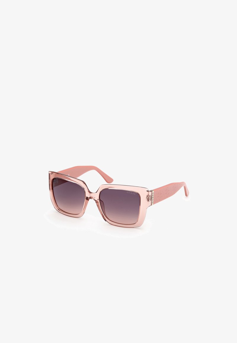 Lunettes de soleil carrées avec une monture rose translucide et des verres gris foncé dégradés. Accentué par un détail de logo sur les branches.