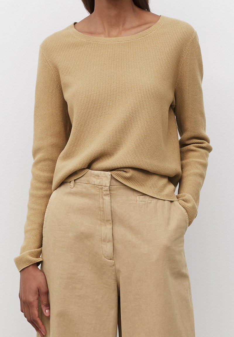 Beige värry neulottu pusero, jossa leveä pyöreä pääntie, pitkät hihat ja rento istuvuus, yhdistetty vaalean sävyisiin pellavahousuihin.
