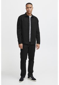 Black button-up jacket with two chest pockets, worn over a gray shirt. Paired with black pants and black and white sneakers.