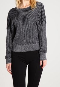 Svart och silverrandig tröja med långa ärmar, bred halsringning och texturerat tyg. Kombinerad med svarta slim fit byxor.