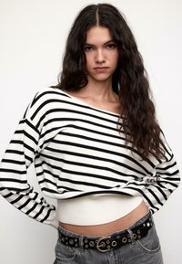 Gestreepte trui met brede boothals, zwart-witte kleuren, zachte textuur. Gecombineerd met hooggetailleerde jeans en een zwarte riem met zilveren gespsluiting.