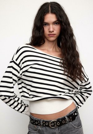 Prugasti džemper s širokim ovratnikom u obliku čamca, crno-bijele boje, mekane teksture. Uparen s trapericama visokog struka i crnim remenom sa srebrnim kopčama.