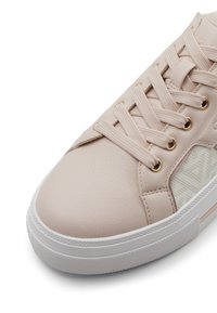 Baskets rose clair avec un dessus en cuir texturé, semelle en caoutchouc blanc, œillets dorés et panneau latéral à motifs. Les lacets sont passés à travers les œillets.