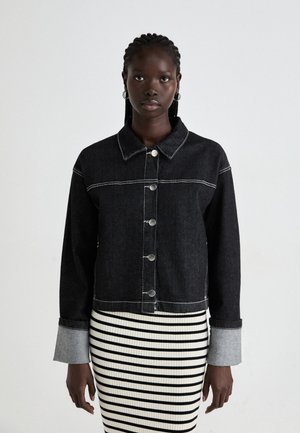 Black denim jacket with contrast white stitching, button front, and collar. Paired with a black-and-white striped ribbed skirt.