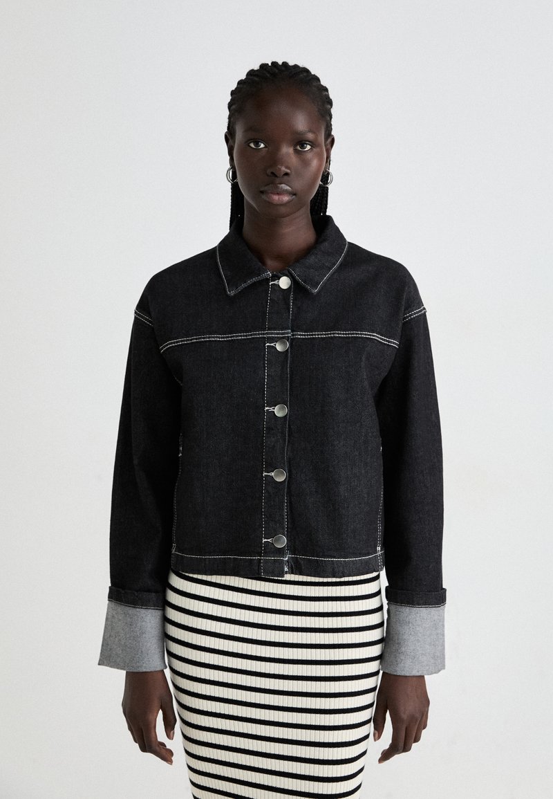 Black denim jacket with contrast white stitching, button front, and collar. Paired with a black-and-white striped ribbed skirt.