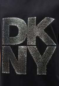 Tecido preto com letras grandes em estilo bloco, feitas de contas prateadas, formando a palavra "DKNY".