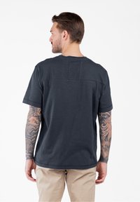 Camiseta de manga corta en gris oscuro con un cuello redondo, que presenta una costura horizontal en la parte posterior y un ajuste holgado. Textura similar al algodón.