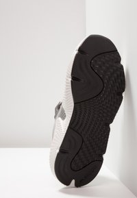 Sko med gummisula som har en strukturerad svart undersida och vit mellansula, designad med en grå meshöverdel och metalliska accenter.