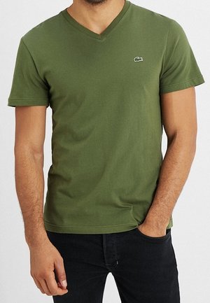 Oliwkowa bawełniana koszulka z dekoltem w serek i krótkimi rękawami, ozdobiona małym logo Lacoste na lewej piersi.