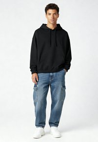 Felpa nera con cappuccio e tasca frontale, abbinata a jeans cargo azzurri con tasche laterali, e sneakers bianche.