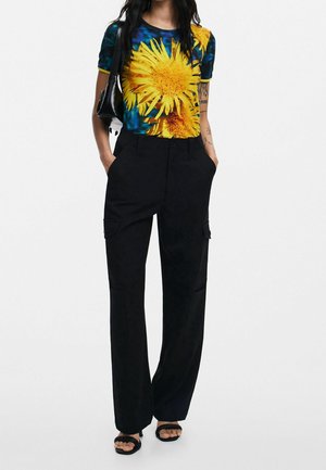 T-shirt graphique avec un imprimé de fleur jaune sur fond bleu, associé à un pantalon cargo noir et des sandales noires.