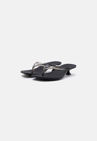 Paire de sandales tongs noires avec petits talons et brides en plastique translucide sur semelles texturées, présentées sur fond blanc.