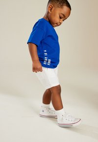 Blue cotton t-shirt with white text, paired with white shorts and white sneakers. The design features short sleeves and a relaxed fit.