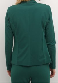 Chaqueta verde ajustada con mangas largas, cuello con muesca y pinzas en la espalda. Tejido suave con un corte estructurado, sin herrajes ni patrones visibles.