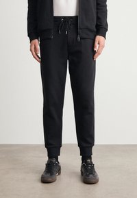 Svarta sweatsbyxor i mjukt tyg med elastisk midja, utrustade med dragsnören, sidofickor och avsmalnande anklar.