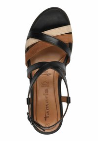 Sandale en cuir noir et brun avec un design à lanières croisées, semelle intérieure beige et une sangle de cheville réglable. Texture lisse et bout arrondi.