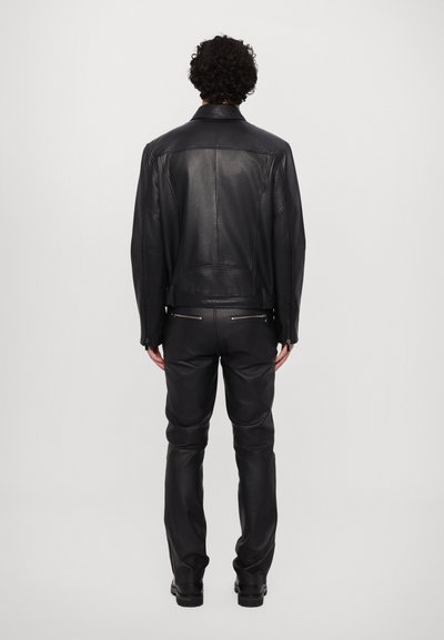 Zwarte leren jas met een aansluitend ontwerp, achternaden en minimalistische ritsdetails, gecombineerd met zwarte leren broeken en laarzen.