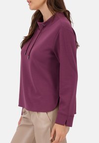 Paarse sweatshirts met hoge hals, trekkoorddetails en lange mouwen. Heeft een afgeronde onderkant en een zachte, gewatteerde stof.