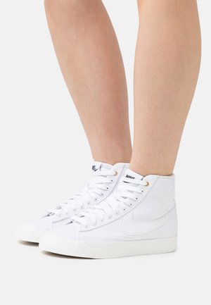 Vita hög-top sneakers i canvas med en texturerad yta, med guldöglor, vita snören och en gummisula.