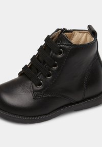 Botas de cuero negras hasta el tobillo con cordones en la parte frontal, ojales metálicos y un acabado texturizado. Cuentan con una cremallera lateral para facilitar el uso.