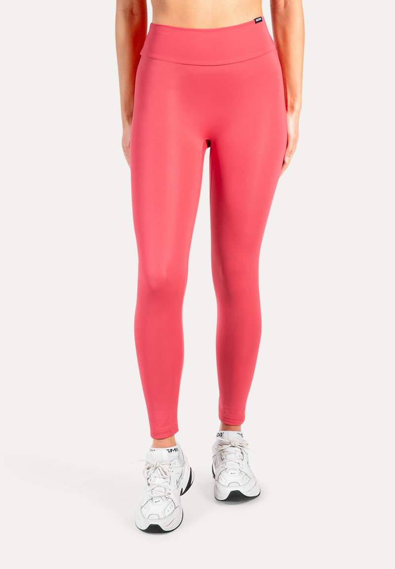 Leggings met hoge taille en aansluitende pasvorm in felroze, gemaakt van glad, rekbaar materiaal. Gecombineerd met witte sportschoenen.