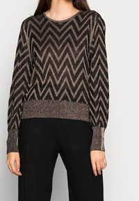 Svart och guld chevronmönstrad tröja med långa ärmar och ribbad nederkant, med knappdetaljer på ärmsluten. Texturerad, skimrande tyg.