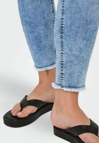 Melnas platformas čības ar platām siksnām un gludu tekstūru, kopā ar gaiši zilām džinsām ar sviestāli izgriezumu, kas parāda vieglu izbalēšanu.