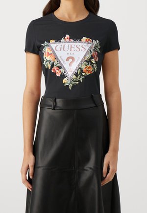 Sort tætsiddende t-shirt med farverigt blomsterdesign og "GUESS U.S.A." trekantet logo, kombineret med høj talje sort lædernederdel.