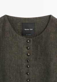 Dunkelolivgrünes, strukturiertes Stoffoberteil mit rundem Ausschnitt und sechs kleinen, runden schwarzen Knöpfen in der vorderen Mitte.