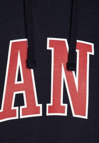 Felpa blu navy con grandi lettere rosse in stampa blocco che formano la parola "MAN." Il materiale è un tessuto liscio e texturizzato con coulisse.