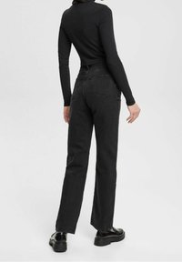 Pantalones vaqueros negros con un diseño de pierna recta, que cuentan con una cintura alta, bolsillos traseros y una textura mate, combinados con una blusa ajustada de manga larga negra.