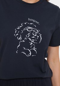 Marinblå bomull t-shirt med en vit kontur grafik av en hund med glasögon, med texten "bonjour.." ovanför illustrationen.