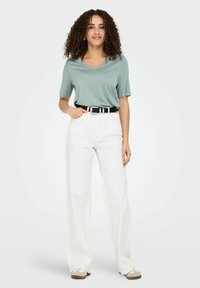 Top de cuello en V azul claro combinado con pantalones de tiro alto de pierna ancha blancos y un cinturón negro; modelo usando zapatos de lona beige con detalles.