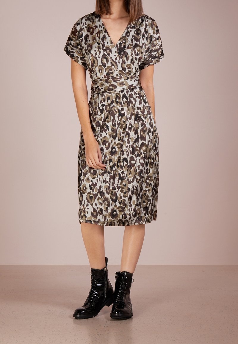 Leopardmuster Wickelkleid in sanften Grüntönen und Brauntönen, kurze Ärmel, V-Ausschnitt, tailliert, mit zwei seitlichen Taschen. Getragen mit schwarzen Stiefeln im Combat-Stil.