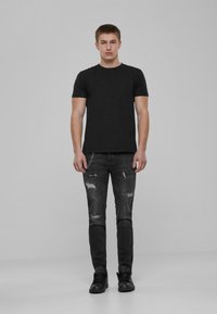 Musta puuvillapaita yhdistettynä kulutettuihin mustiin farkkuihin, joissa on revittyjä yksityiskohtia ja hopeaketju, täydentäen asua mustilla saappailla.