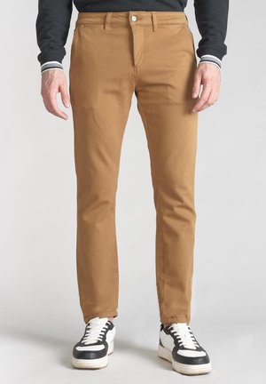 Tan cotton trousers with a slim fit, featuring a front pocket and a single button closure, paired with black and white sneakers.