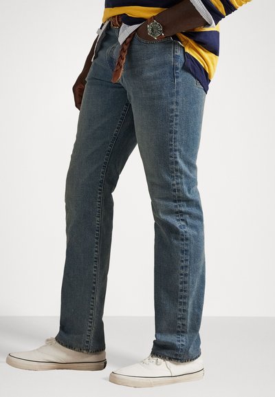 Blå denimbukser med lige pasform, med subtil falming, fem lommer og parret med hvide sneakers og et brunt flettebælte.