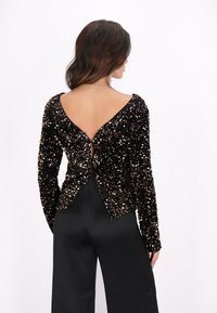 Czarny top z cekinami, z długimi rękawami, z tylnym dekoltem w kształcie litery V i dopasowanym krojem. Połączony z czarnymi satynowymi spodniami, które eksponują elegancką fakturę.