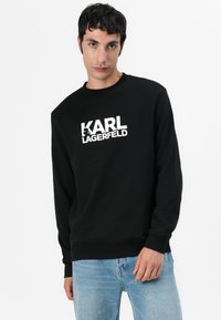 Schwarzer Sweatshirt aus Baumwolle mit langen Ärmeln, gerippten Bündchen und Rundhalsausschnitt. Mit einem großen weißen "KARL LAGERFELD" Logo auf der Vorderseite.