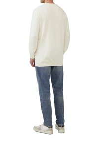 Cremfarbener Strickpullover mit langen Ärmeln, Rundhalsausschnitt und Rippbündchen. Kombiniert mit ausgewaschenen blauen Jeans und hellen Sneakers.