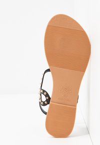 Sandal nero con accenti di borchie, suola in gomma testurizzata e logo del marchio. Design piatto con punta aperta e dettaglio della cinghia alla caviglia.
